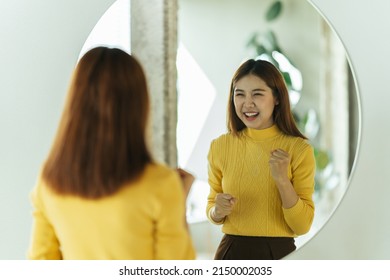 A young Asian woman talks to herself through a mirror to build her self-confidence and empower herself. - Shutterstock ID 2150002035