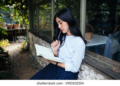 Young Asian Woman Think Of The Concept Before Write It On A Book. Woman Novel Writer Thinking About The Next Chapter Of The Story.