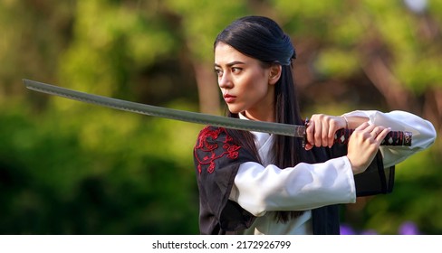 Young asian woman in traditional kimono trains in a fighting stance close-up portrait with katana sword samurai warrior girl in green summer garden 