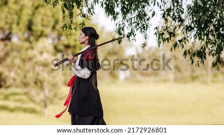 Young asian woman in traditional kimono portrait with katana sword samurai warrior girl walks through the autumn garden