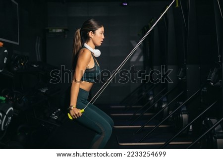 A young Asian woman training with a Nordic ski machine inside a gym.