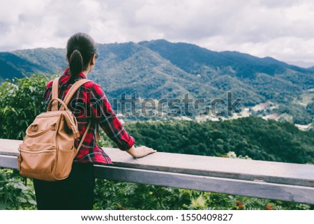 Young Asian woman traveler with backpack at beautiful forest looking towards mountain ranges covered by evergreen cold rain-forests in Thailand. Portrait concept. Travel holiday relaxation concept.