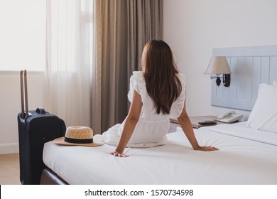 Young Asian Woman Traveler With Luggage Sitting And Relaxing On The Bed In Hotel Room