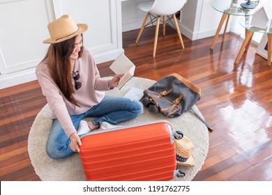 Young Asian Woman Traveler Prepare Things Into Orange Suitcase For Holiday Vacation At Home.backpacker Travel Concept