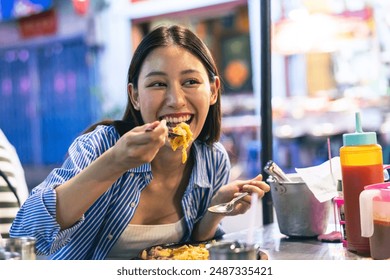 Young Asian woman traveler tourist eating Thai street food in China town night market in Bangkok in Thailand - people traveling enjoying food culture concept - Powered by Shutterstock