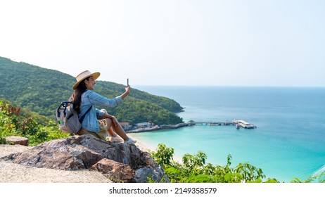 Young Asian woman traveler using mobile phone taking selfie while solo travel on tropical island mountain in summer sunny day. Cheerful female enjoy outdoor lifestyle in holiday beach vacation trip - Shutterstock ID 2149358579