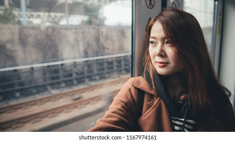 Young asian woman traveling by train looking at window and exploring the city.
