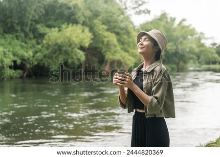Young asian woman traveller drinking coffee in nature forest background. Happy Beautiful woman living middle of a lot of tree. Breathing the fresh air on her vacation weekend holiday trip.