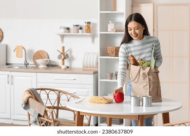 Young Asian woman unpacking fresh products from market at table in kitchen - Powered by Shutterstock