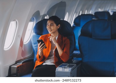 Young Asian woman uses mobile phone to check news information Sitting near the window in business class, airplane class during flight, travel and business concept - Powered by Shutterstock