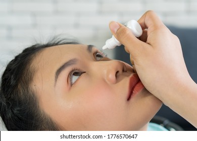 Young Asian Woman Using Artificial Tear And Antibiotics To Drop In Her Eye To Treat Dry Eyes From Contact Lens Wearing And Infection. Healthcare And Medical Concept