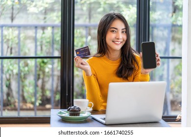 Young Asian woman using credit card and presenting mobile phone for online shopping in coffee shop or coworking space, coffee cup, technology money wallet and online payment concept,credit card mockup