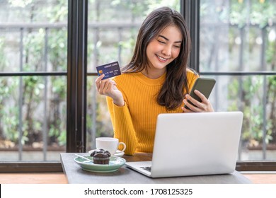 Young Asian Woman Using Credit Card And Mobile Phone For Online Shopping In Coffee Shop Or Coworking Space, Coffee Cup, Technology Money Wallet And Online Payment Concept, Credit Card Mockup