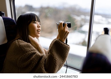 Young Asian woman using digital camera taking picture of beautiful view out of the window during travel on train at sunset. Attractive girl travel Japan on railroad transportation on winter vacation. - Powered by Shutterstock