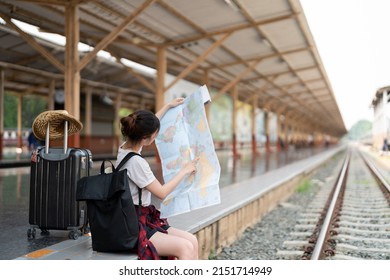 Young Asian Woman Using Generic Local Map, Siting Alone At Train Station Platform With Luggage. Summer Holiday Traveling Or Young Tourist Backpack Traveler Concept