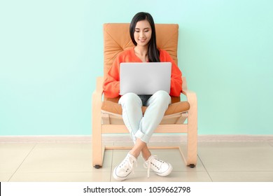 Young Asian Woman Using Laptop In Armchair, Indoors