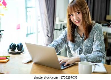 家庭で働くためにノートパソコンと携帯電話を使い、自宅の顧客とオンラインでコミュニケーションを取るアジアの若い女性。快適なオフィス、リモートワーク、またはコールセンター。Eラーニングのコンセプト。