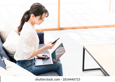 Young Asian Woman Using A Laptop Pc And A Smart Phone In Living Room.