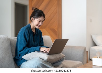 Young Asian Woman Using Laptop In The Sofa With A Happy Face Standing And Smiling With A Confident Smile Showing Teeth