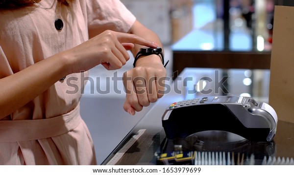 Young Asian woman using mobile phone - smartwatch\
to purchase product at the point of sale terminal in a retail store\
with near field communication nfc  radio frequency identification\
payment