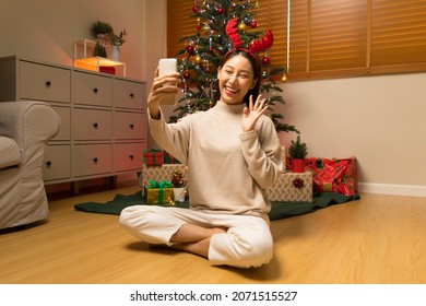 Young Asian woman using smart phone video call talking with friend or boyfriend. Christmas tree decorated with ornament in living room at home. Christmas and New Year holiday festival. - Powered by Shutterstock