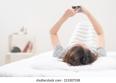 Young Asian Woman Using A Smart Phone On A Bed.