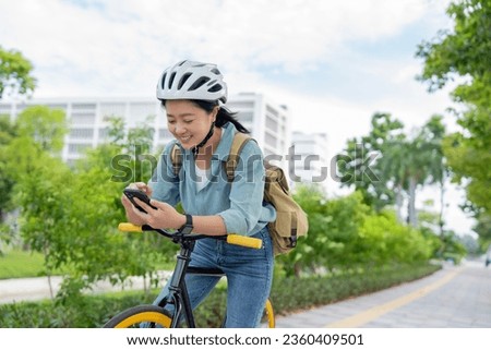 Young asian woman using smart phone on a bicycle in the park. technology and lifestyle concept