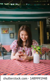 Young asian woman using smartphone waiting for her friend to come at restaurant, Attractive woman waiting for a phone call or message from her boyfriend.