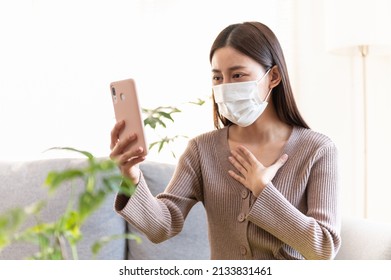 Young Asian woman using smartphone connect video call talking with doctor from hospital consult about sickness symptom during home isolation from covid pandemic. Health care and Telehealth technology.