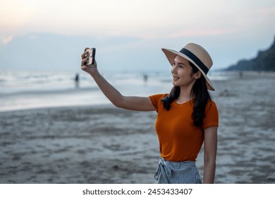 Young asian woman using smartphone to take a photo of seaview while sunset time. Traveler female Relaxing on holiday weekend vacation time. Pick up cell phone to capture the impression - Powered by Shutterstock