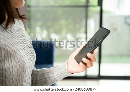 Young asian woman using smartphone sitting on blue sofa in the house. Businesswoman with typing cellphone sending message while sitting on couch