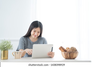 Young Asian Woman Using Tablet At Home And Having Breakfast In The Morning .She Reading On Tablet.