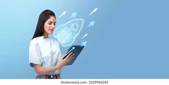 Young asian woman using tablet, glowing rocket hologram hud, empty blue background. Concept of business technology, startup, investment and growth - Powered by Shutterstock