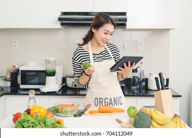 Young Asian Woman Using A Tablet Computer To Cook In Her Kitchen