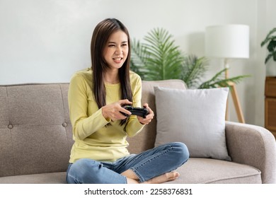 Young asian woman is using video game control joystick to playing games with enjoyment while sitting on the big comfortable sofa in living room at home. - Shutterstock ID 2258376831