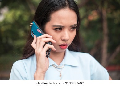 A young asian woman is visibly nervous listening to the demands of a scammer on her phone. A asian lady being blackmailed