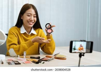 Young Asian Woman Vlogging About Cosmetics Skin Care Items Products On Table With Her Video Camera And Demonstrates Product Use And Reviews For Her Online Blog Channel.