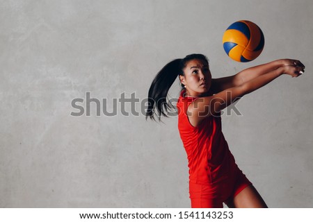 Young Asian woman volleyball player in red uniform takes ball