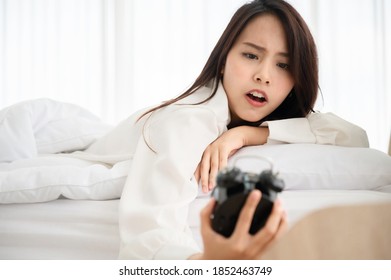 Young Asian Woman Wake Up Late In Morning. She Shocking And Excited Looking At Alarm Clock On Bed