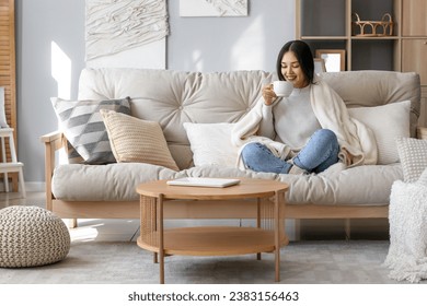 Young Asian woman with warm plaid drinking tea at home - Powered by Shutterstock