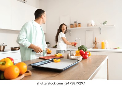 Young Asian woman washing bell pepper and her husband cooking in kitchen - Powered by Shutterstock