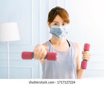 Young asian woman wear mask and doing exercises at home with dumbbells - Powered by Shutterstock