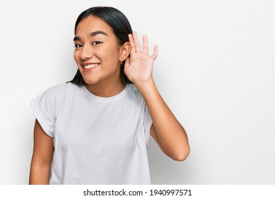 Young Asian Woman Wearing Casual White T Shirt Smiling With Hand Over Ear Listening An Hearing To Rumor Or Gossip. Deafness Concept. 