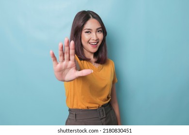 Young Asian woman wearing casual t-shirt over blue isolated background doing stop sign with palm of the hand.  - Powered by Shutterstock