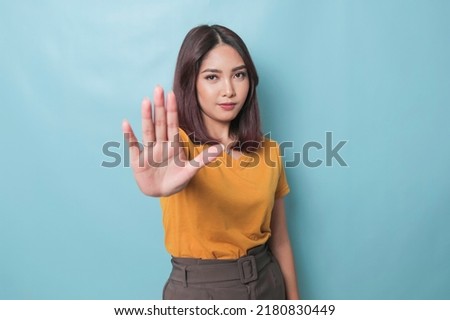 Young Asian woman wearing casual t-shirt over blue isolated background doing stop sign with palm of the hand. 