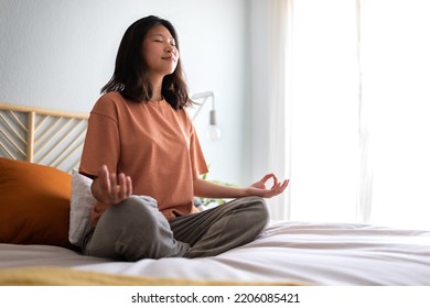 Young Asian Woman Wearing Comfortable Clothes Meditating On The Bed In The Morning To Clear Mind. Copy Space.