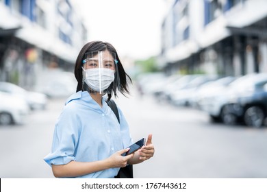 Young Asian Woman Wearing Face Mask Under Face Shield, Is Standing At A Domestic Street. Concept New Normal Of Commuters After Covid-19 Epidemic