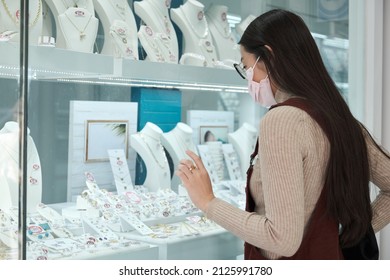 Young asian woman wearing face mask looking at a jewellery showcase at a city street. - Powered by Shutterstock