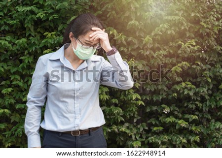 Young asian woman wearing glasses and face hygienic mask protect filter pm2.5 anti pollution, anti smog and viruses with headache,standing with green background. Air pollution, environmental concept.