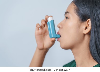 Young Asian woman wearing green t-shirt using asthma inhaler isolated on white background, indoors, studio shot. - Powered by Shutterstock